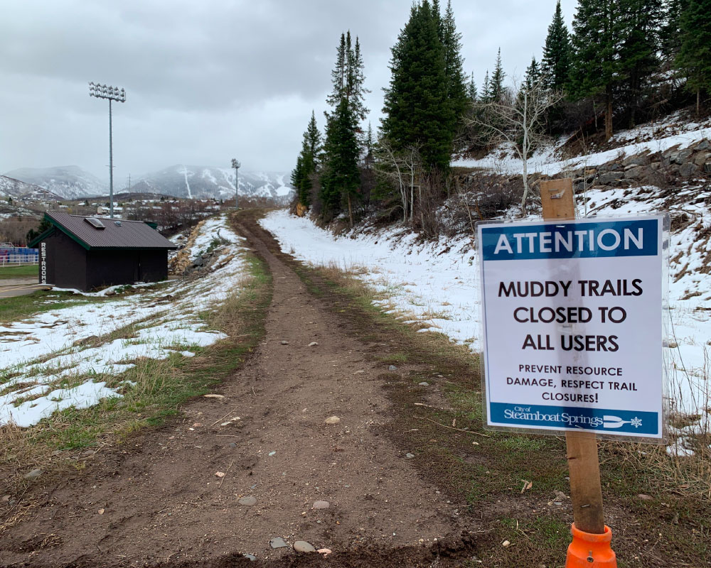 Muddy trail with trail closed sign and snow on the ground